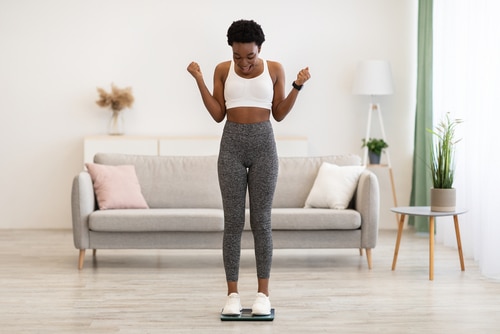 Woman celebrating weight loss on a scale in a living room.